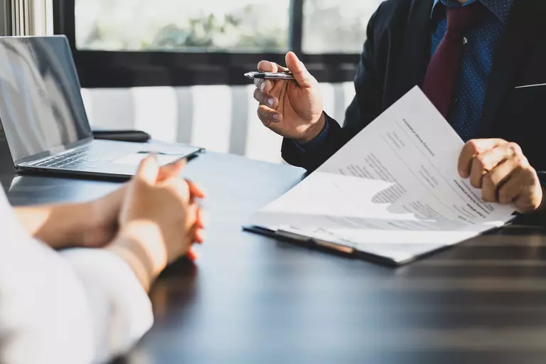 A professional conversing with someone across a table with a document between them.