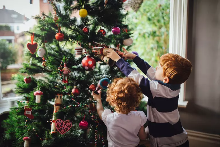 Two boys adding ornaments to a Christmas tree.