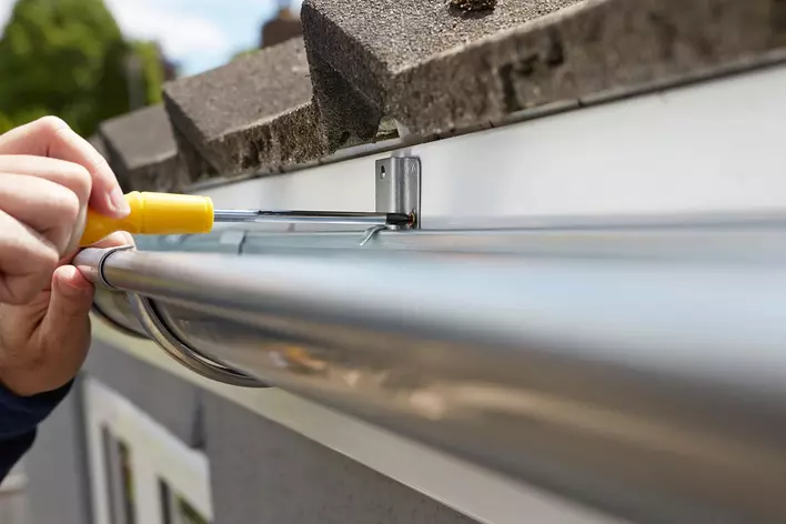 A close-up of a person screwing in a gutter guard on a house