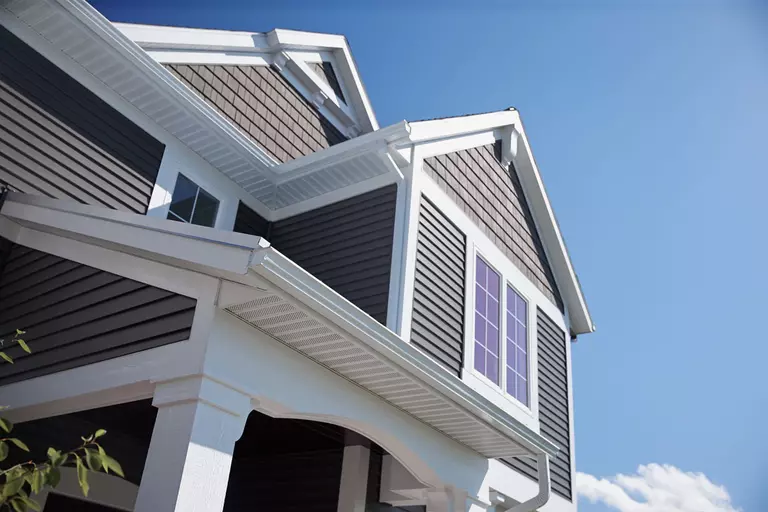 The upper level of a vinyl siding home zoomed in on the gutters, energy-efficient windows, and freshly painted siding with white exterior trim.