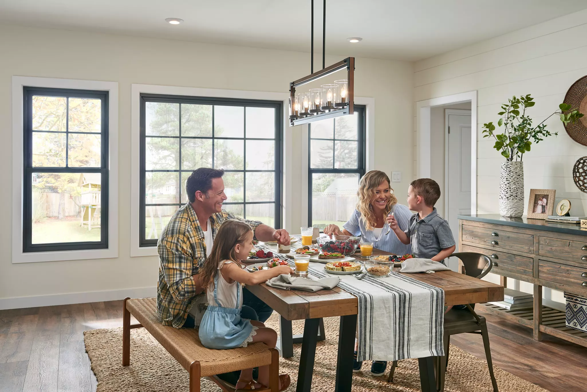 Family eating breakfast in a bright dining room with large windows.