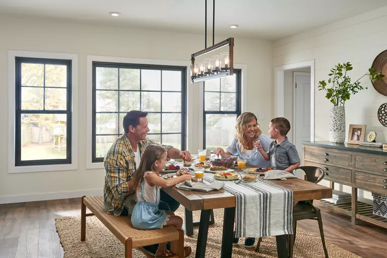 Family seated around a dining table with double-hung and fixed windows in the background.