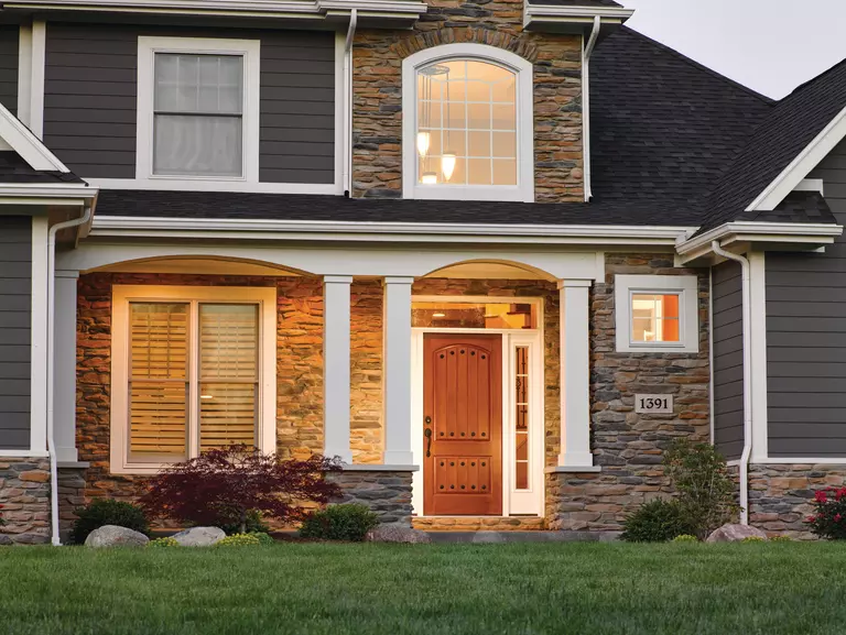 The entryway of a home with sidelites, a deep transom, a woodgrain entry door, and stacked stone detailing.