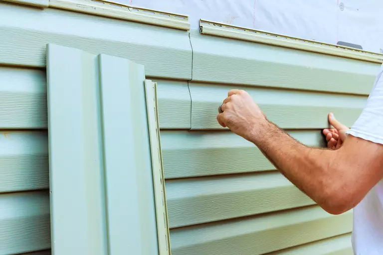 Person installing mint colored vinyl siding on a home.