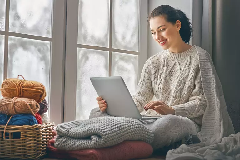 A woman bundled up on her laptop, sitting in a window seat overlooking the snowy
outdoors.