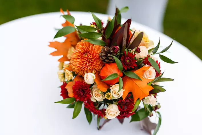 A fall seasonal bouquet with aster flowers, dry leaves, and pinecones set on a white tablecloth.