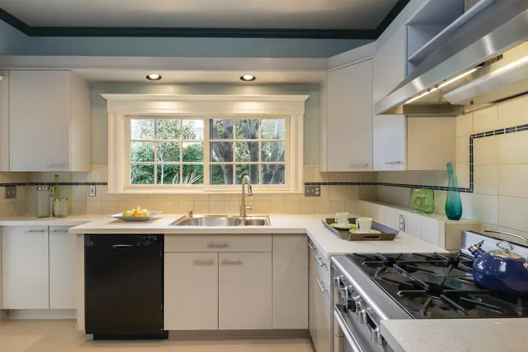 A kitchen with white cabinets and a sliding window above the sink.
