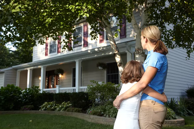 Mother hugging her child in front of a home.