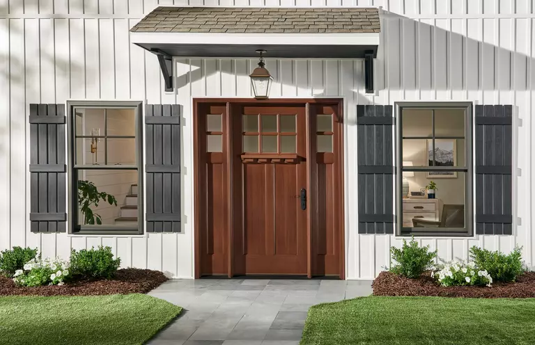 White home with wood grain entry doors featuring windows with gray exterior window shutters.