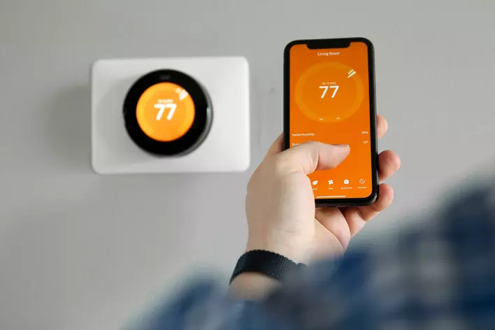 A man using an app on his phone to control his energy-efficient smart thermostat.