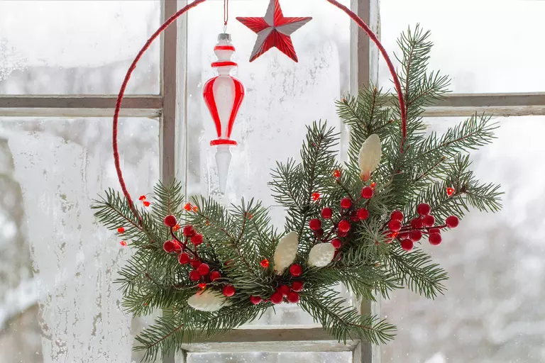 A minimalist holiday wreath with holiday berries in front of a window with frosted glass.