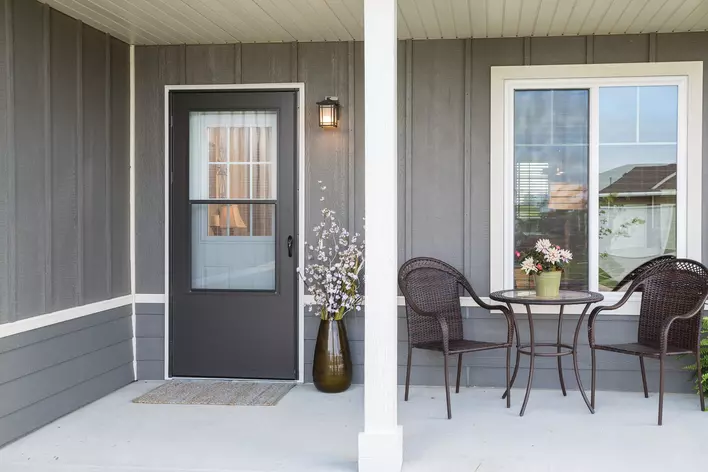 A gray storm door on the porch of a gray-and-white home with patio furniture nearby.