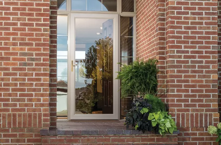 A full view storm door on a brick building. The storm door has a wide, crystal-clear glass front.