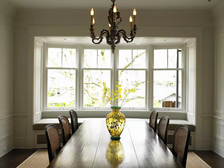 A dining room table with a four-panel bow window and seat.
