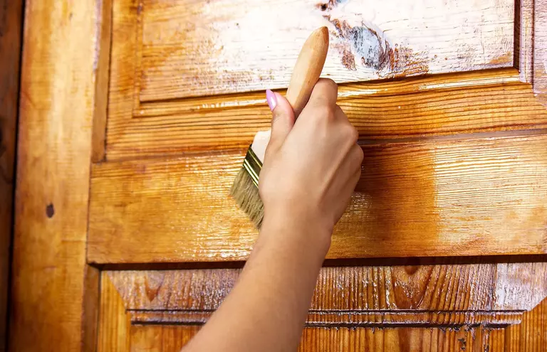 Person using a brush to apply a finish to a wooden door.