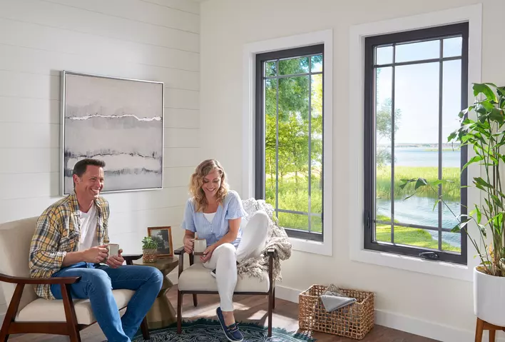 A couple sitting comfortably in a room at home with large energy-efficient windows next to them. 