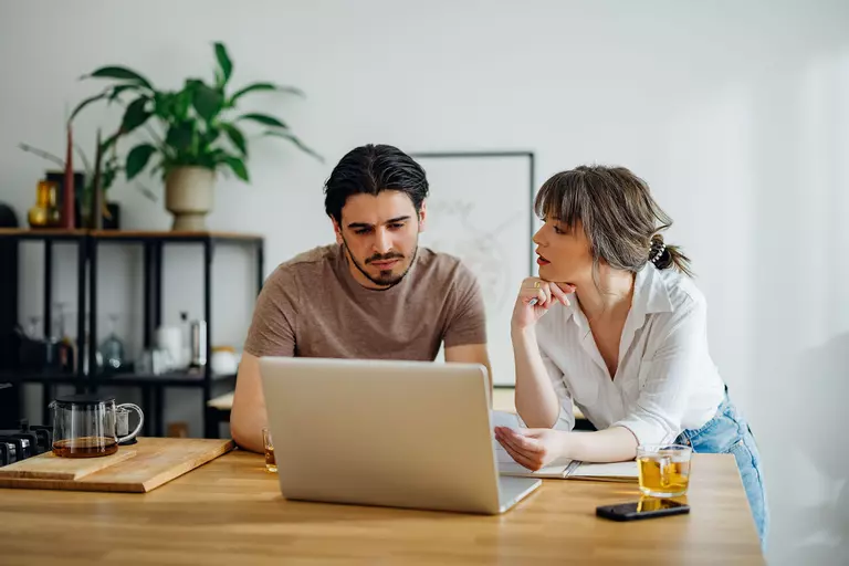 A man and a woman at a table looking at a laptop.