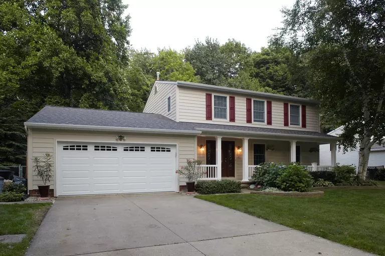 A beige composite siding home with burgundy shutters, a front-facing two-car garage, an open front porch, and a big front yard with simple landscaping.