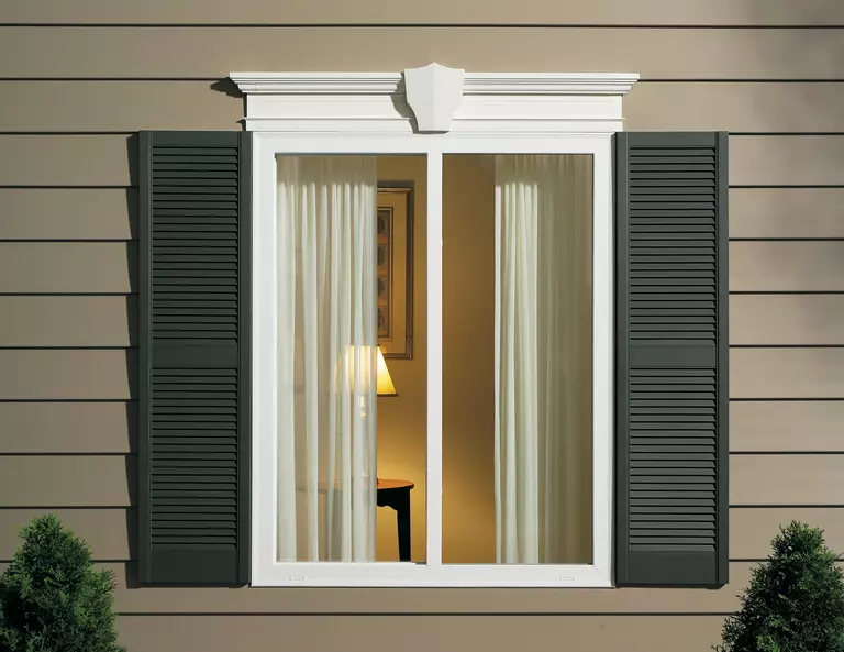 Window with green-colored exterior window shutters on the side of a tan home.
