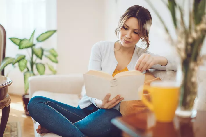 A woman reading a book in her quiet living room that keeps noise out with insulated
windows.