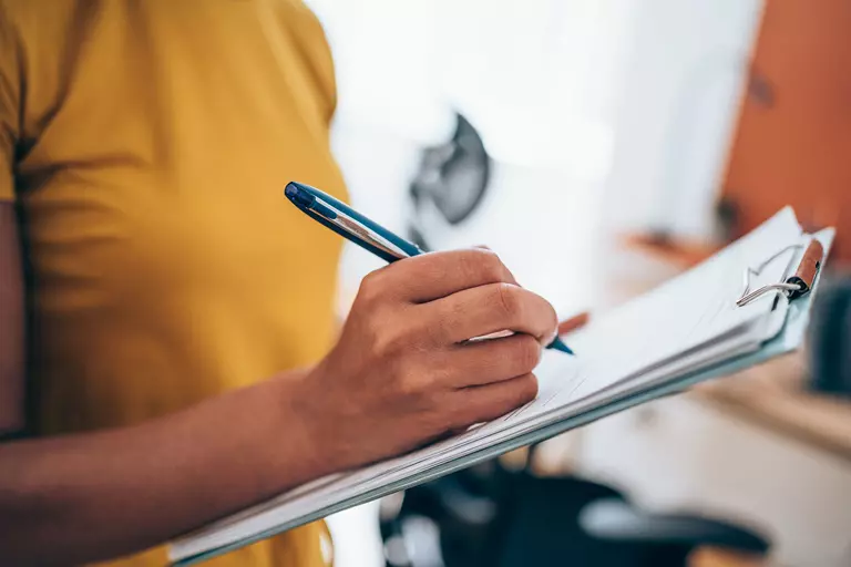 Woman signing a document on a clipboard.