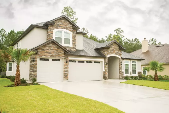 Gray long panel garage door with clear windows installed on a two-story stone home