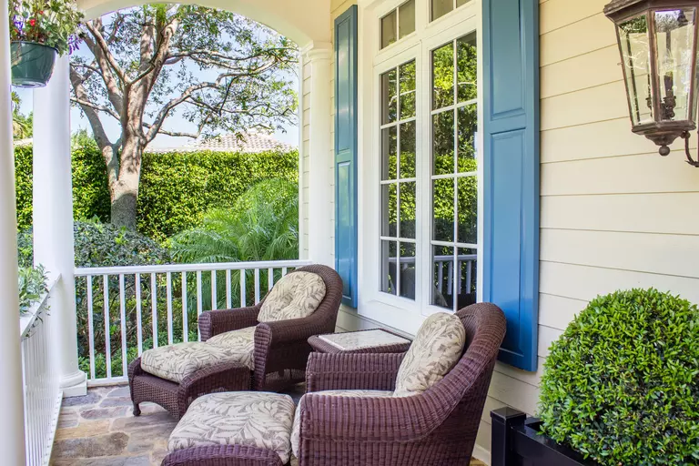 A home with a pair of front porch seats and light-blue raised panel shutters on the window behind them.