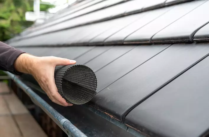 A person installing a gutter guard on the roof of a home