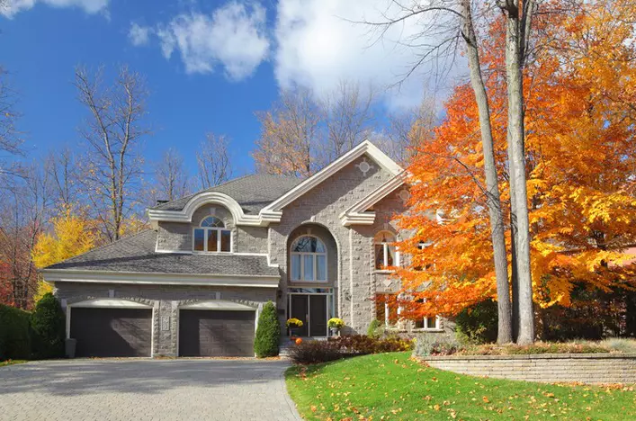 A large, gray brick home with large windows, dark brown accents, and a newly replaced roof.