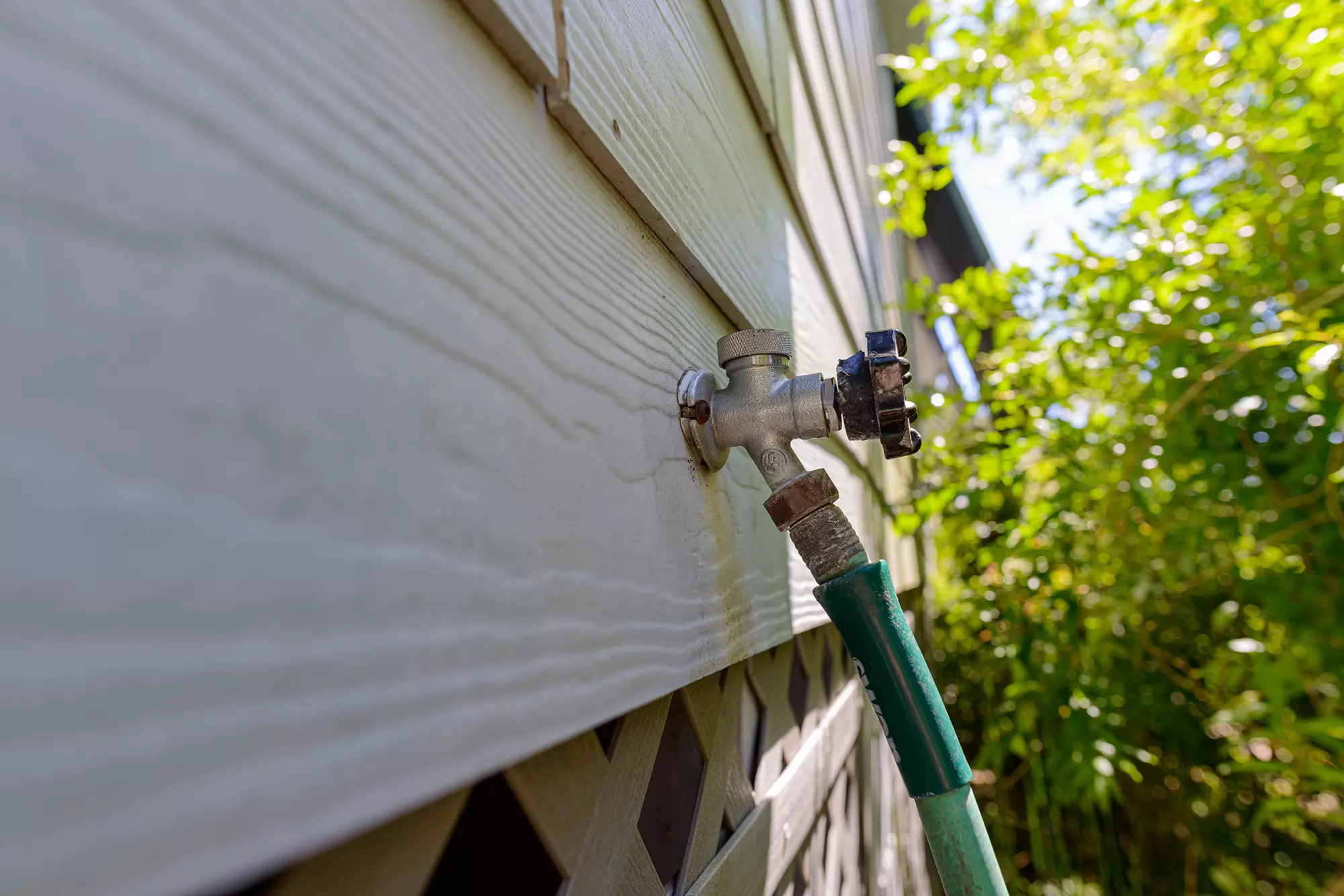 Close-up of a garden hose faucet on the side of a home.