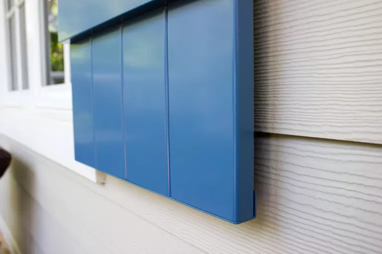 Close-up of a blue shutter framing a white window on a beige house. Some of the best window treatments are those on the exterior of a house. 