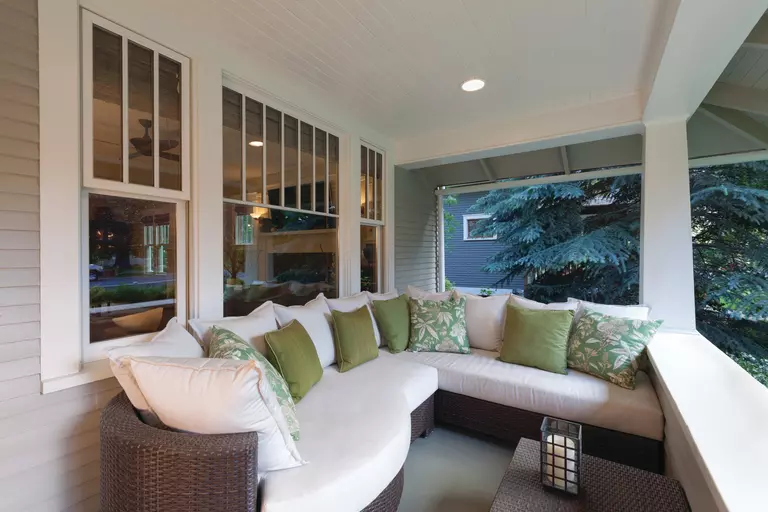 The front porch of a home with an outdoor couch in front of double-hung windows.