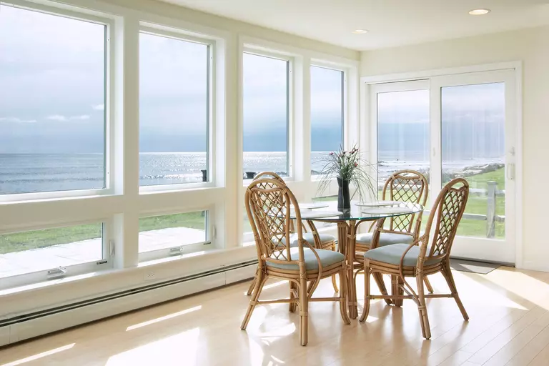 A small dining table with four chairs beside a row of windows and a sliding patio door.