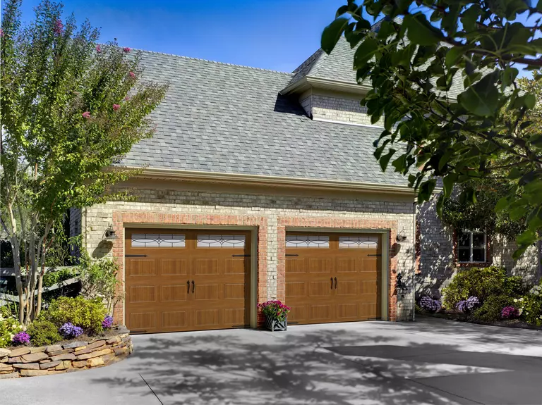 Home garage with decorative glass lites and surrounded by landscaping.