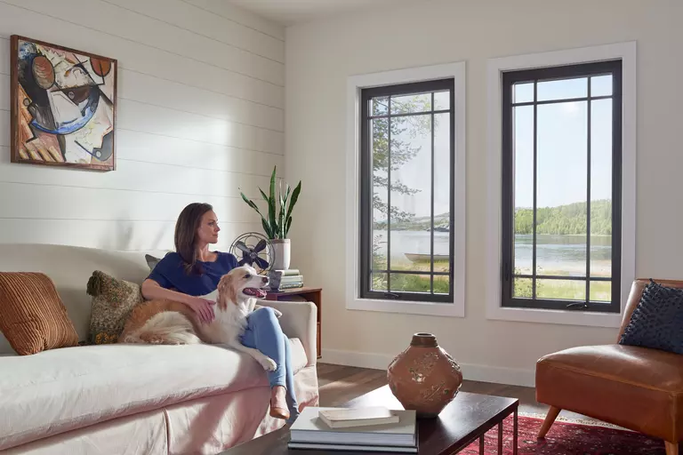 Woman and dog seated on a couch next to similar black casement windows.