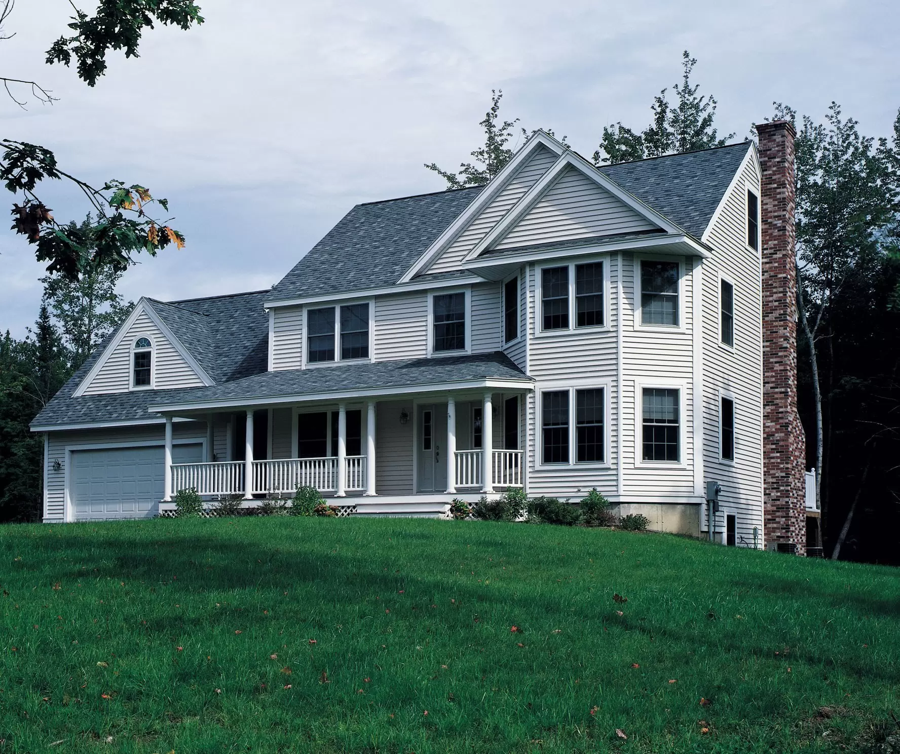 Two-story home with white vinyl siding, a covered front porch, and a brick chimney.