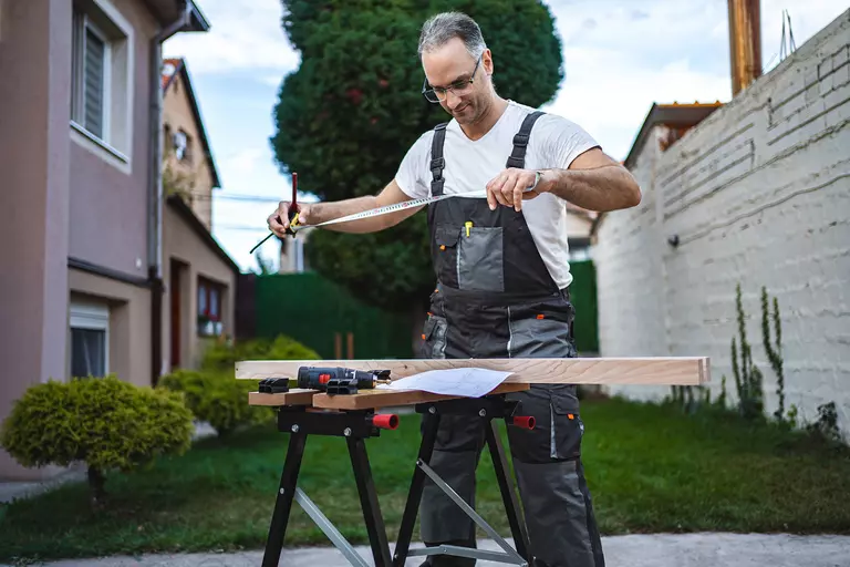 A contractor about to measure a length of timber with a tape measure. He’s preparing to help install new features for a client’s outdoor living space.