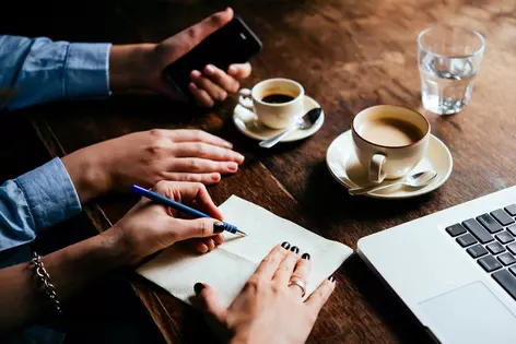people filling out paperwork with coffee and laptop