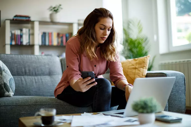 Woman holding a smartphone and using a laptop.