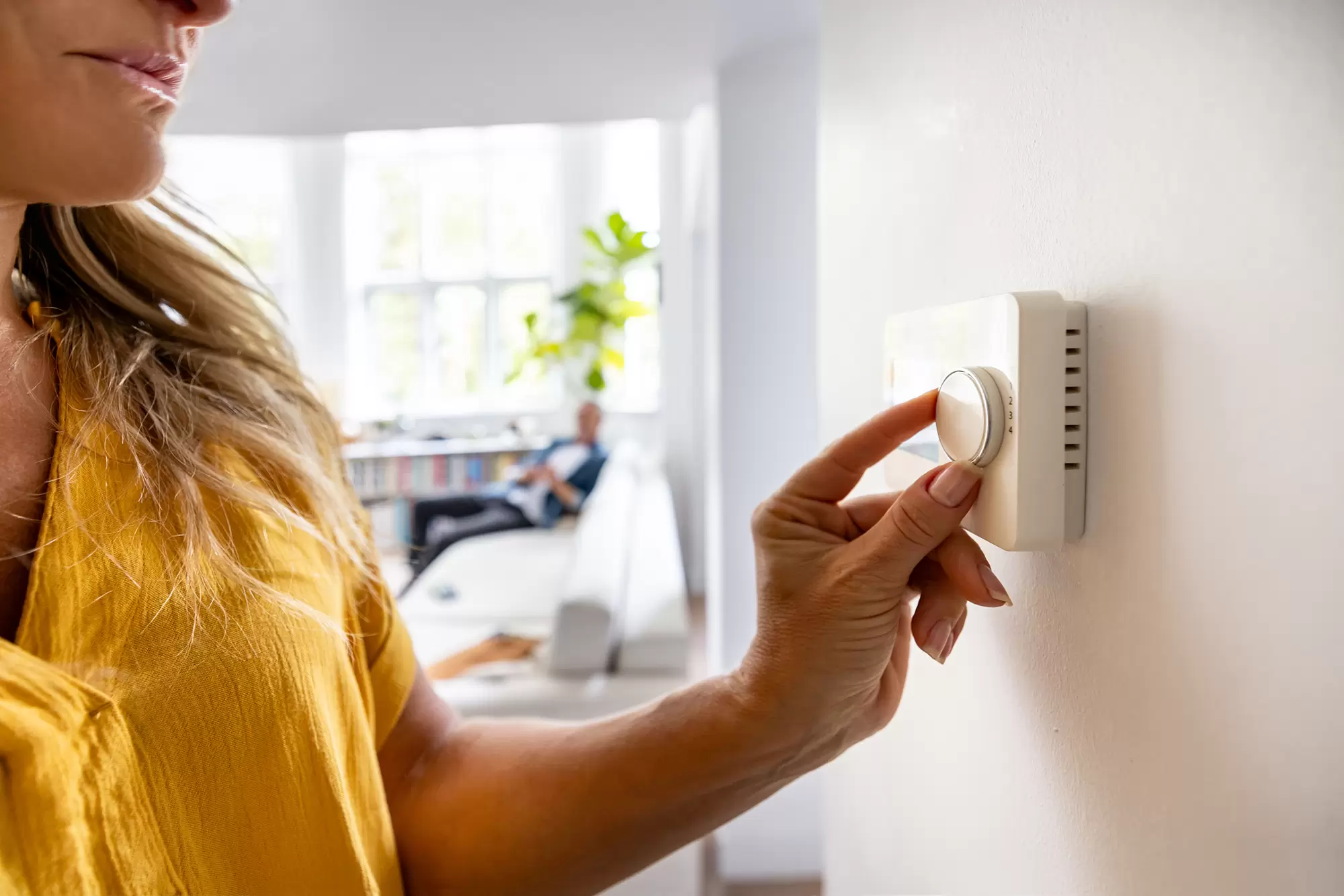 Woman adjusting a wall thermostat.