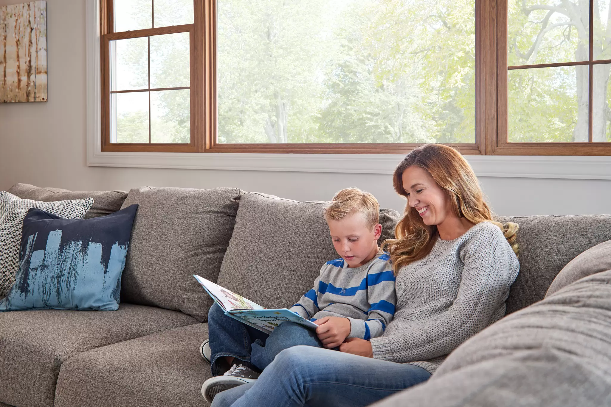 Mother and son reading a book together under a large window.