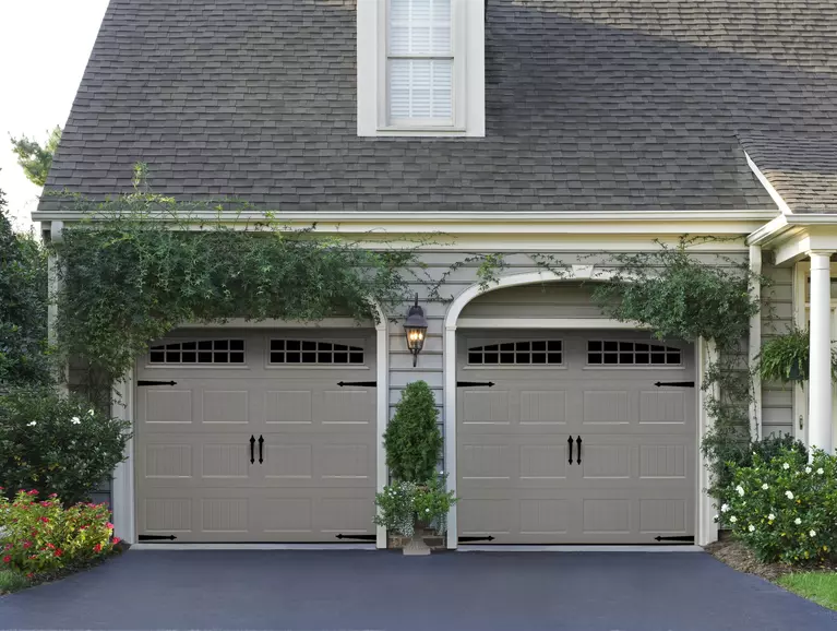 Dual gray wood garage doors covered with ivy.