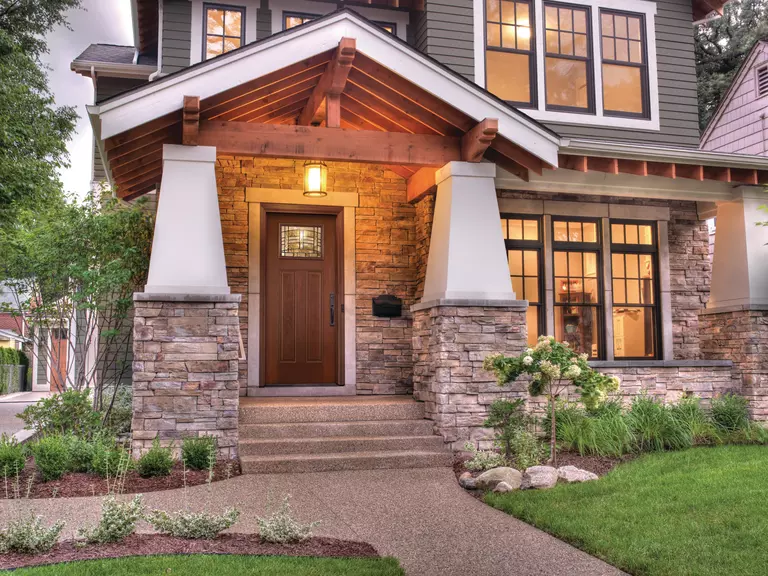 Front exterior of a home with a stone porch and entry door with decorative glass.
