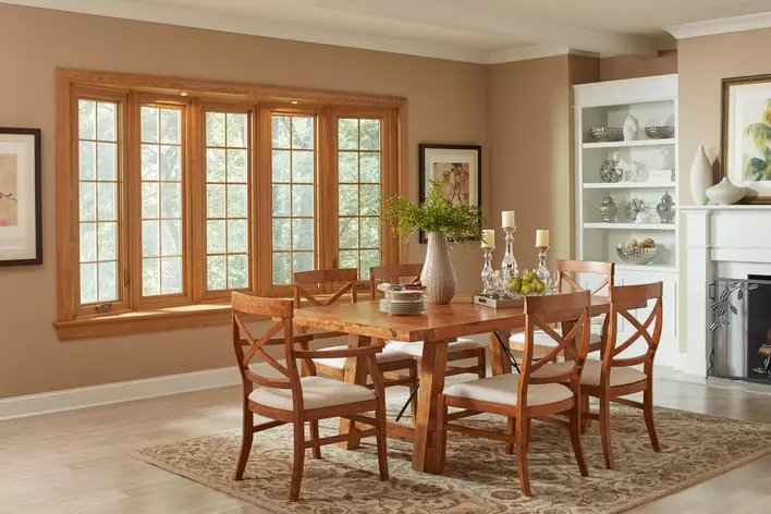 A wooden dining room table with chairs in front of dining room windows