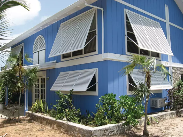 A blue beach home with Bahama shutters set at a 45-degree angle. The shutters can open and close depending on the weather. 
