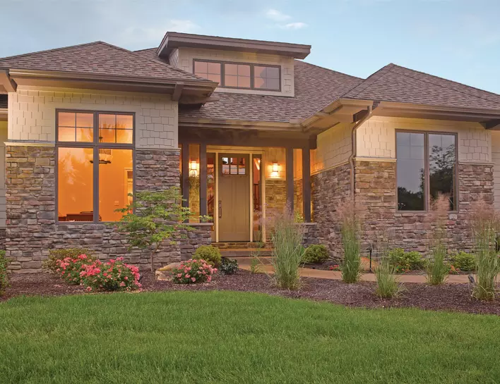 The front of a large house with stacked stone, tan siding, and a fiberglass exterior door<br>at the entrance.