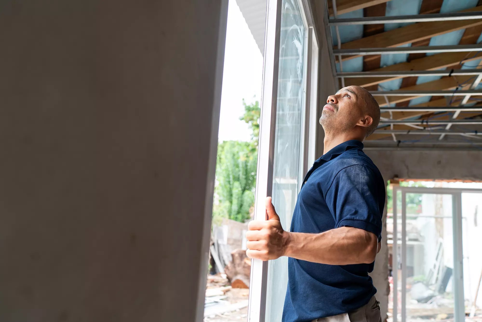 Man installing a large window frame in a building under construction.