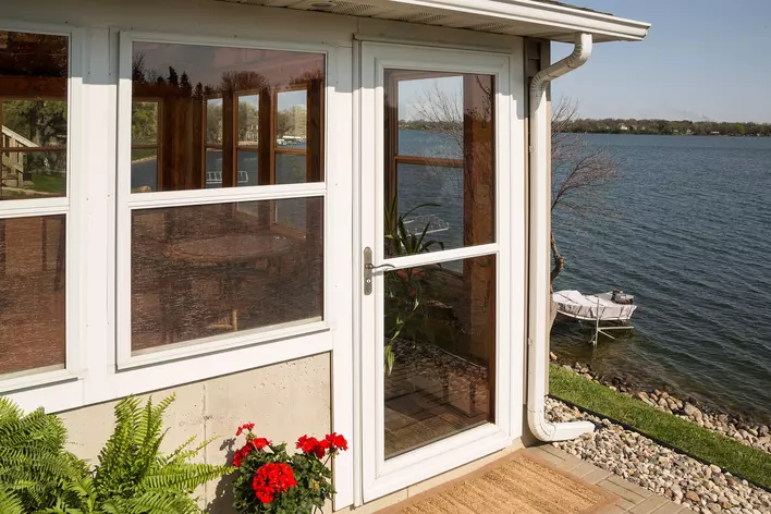 A full view storm door on a home overlooking a lake. A boat is visible on a dock in the distance.