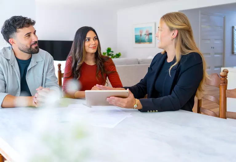 A woman showing a man and a woman a tablet at a table.