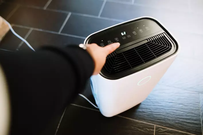 A person reaches out to turn on a dehumidifier to help prevent condensation on
            windows.